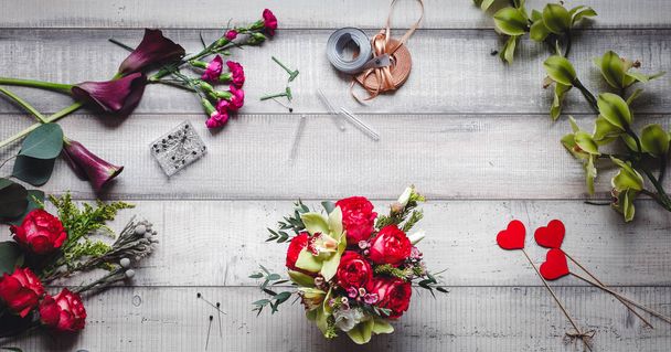 Ramo de rosas rojas, corazones, calas, claveles y cintas sobre la mesa
 - Foto, Imagen