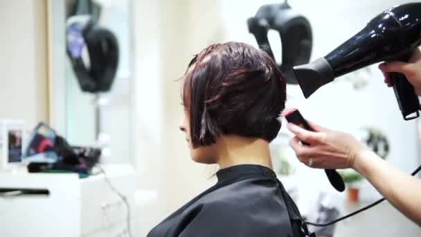 Una joven hermosa mujer secándose el pelo oscuro en los peluqueros, 4K
 - Metraje, vídeo
