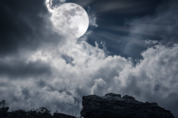 Валун на фоне неба с облаками и красивой полнолунием ночью
 - Фото, изображение