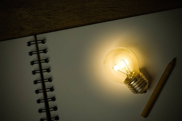 eine Glühbirne mit einem kleinen Bleistift auf einem geöffneten Skizzenbuch - Foto, Bild