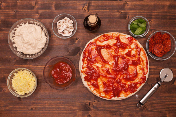 Phasen der Zubereitung einer Pizza - die Tomatensauce auf dem Dou verteilen - Foto, Bild