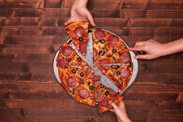 Hands taking pizza slices off the baking pan - 写真・画像