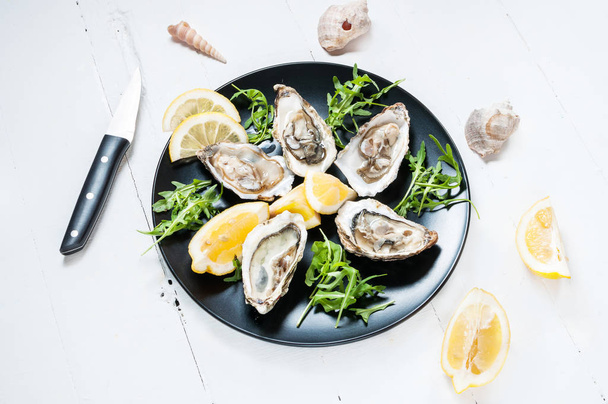 Oysters with lemon fruit on a black plate on a white wood table - Photo, Image