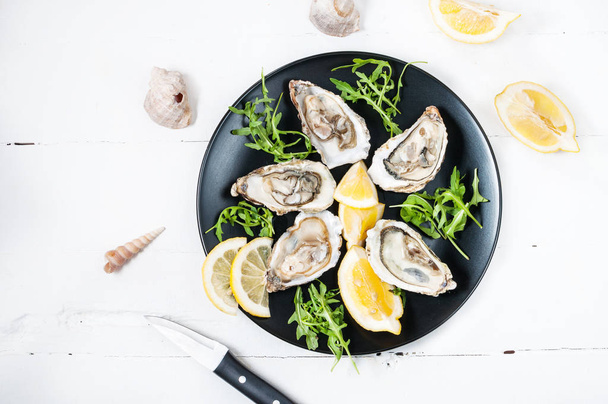 Oysters with lemon fruit on a black plate on a white wood table - Photo, Image