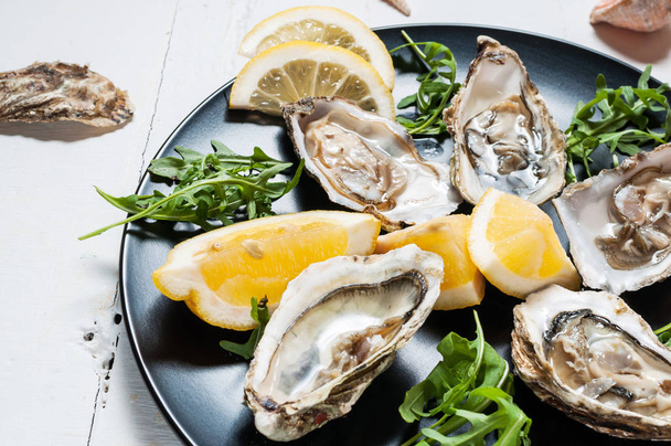 Oysters with lemon fruit on a black plate on a white wood table. - Photo, Image