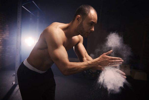 Mann trägt Kreide auf Hände im Fitnessstudio auf - Foto, Bild