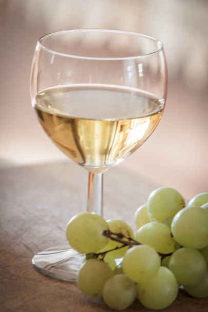 A glass of italian white wine is standing on a wooden tray, near some white grapes - Fotó, kép