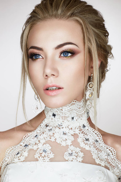 A young girl in the image of a bride in a wedding dress and beautiful shiny earrings. A beautiful model with a bright makeup and perfect skin - Foto, Imagen