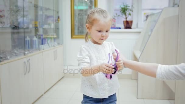 Child - blonde Girl dancing and tries colorful glasses in medical store - shopping in clinic - Imágenes, Vídeo
