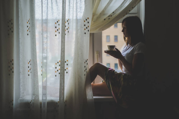 Girl sitting on the windowsill and drinking tea - Valokuva, kuva