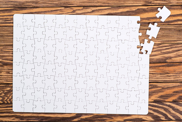 Incomplete white puzzles on wooden table. - Photo, Image