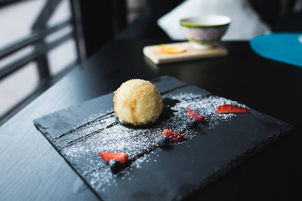 Grilled ice-cream in coconut with sauce on black stone plate. Asian food background. Eating concept. Restaraunt place with wooden table. Copy space for text, design. - Foto, Imagen