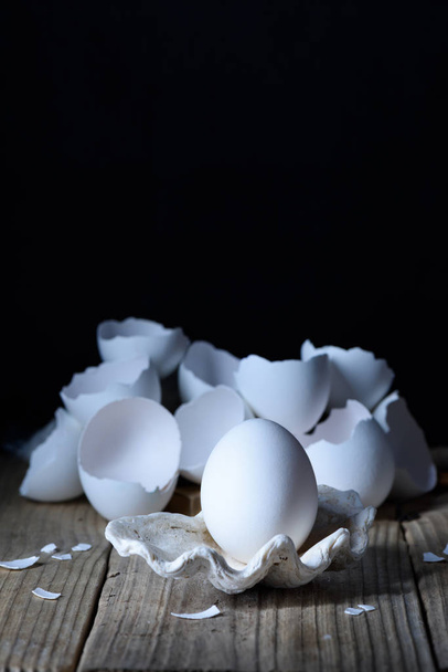 White egg on in a shell in center, cracked eggshell. Design, art, close up.  - Фото, изображение