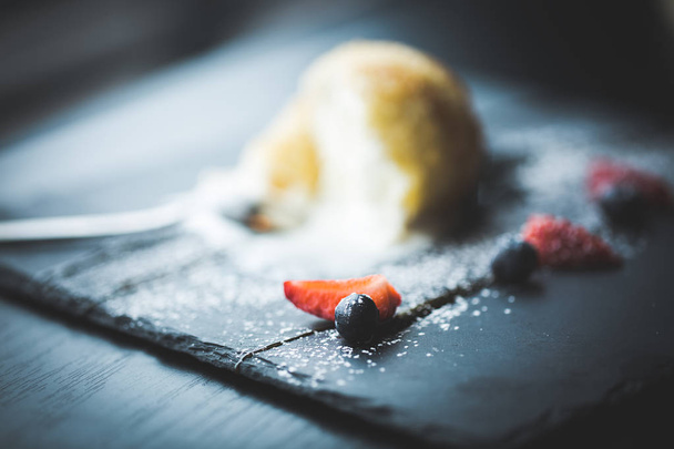 Grilled ice-cream in coconut with sauce and fruits on black stone plate with tea spoon. Asian food background. Eating concept. Restaraunt place with wooden table. Copy space for text, design - 写真・画像