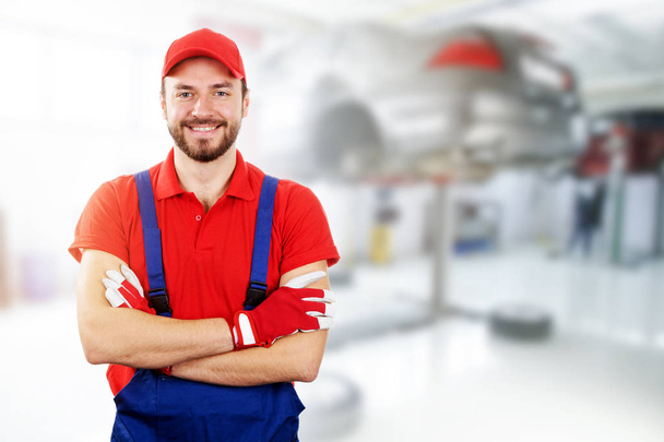 happy auto mechanic standing in car service garage - Zdjęcie, obraz