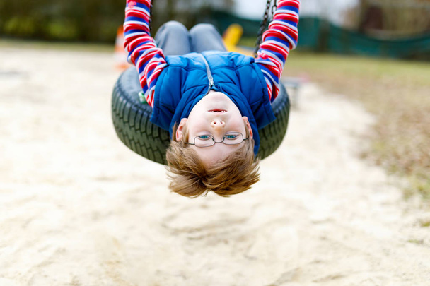 Funny kid boy having fun with chain swing on outdoor playground - Photo, Image