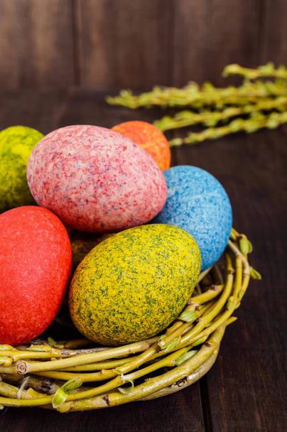 Kleurrijke beschilderde eieren in een nest van twijgen van wilg op een donkere houten achtergrond. Traditioneel voor Pasen. Verticale weergave. - Foto, afbeelding