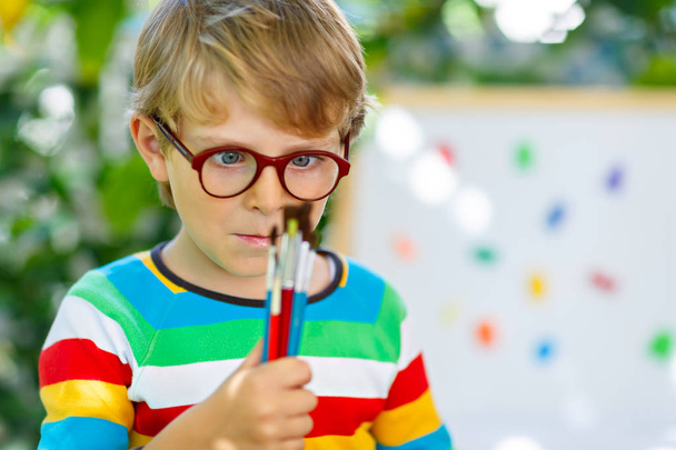 Niño pequeño con gafas sosteniendo el equipo escolar
 - Foto, Imagen