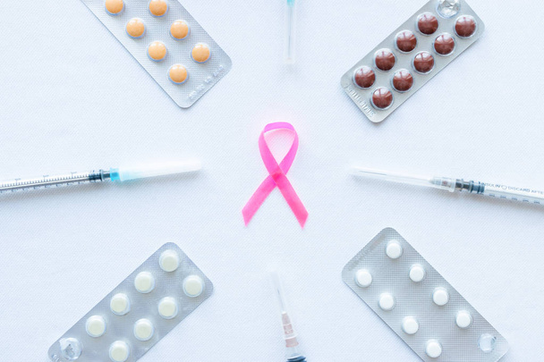 pink ribbon symbol for breast cancer on a white background with syringes and tablets - Zdjęcie, obraz