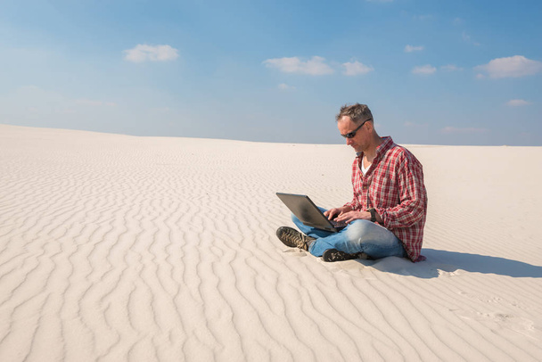 Concerned man with a laptop sits in desert - 写真・画像