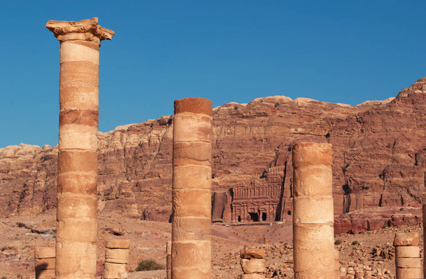 Jordanië: Kings muur met de koninklijke graftombes, funeraire structuren uitgehouwen in de rotswand aan de voet van de berg, gezien door de kolommen van de grote tempel in de verloren stad Petra - Foto, afbeelding