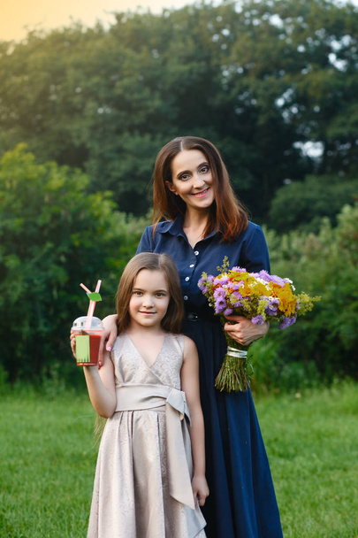 Mom and daughter are walking in a meadow, picking flowers and drinking juice - Foto, imagen