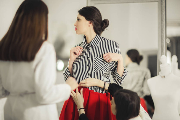 Two fashion designers adjusting red skirt on model in the studio - Фото, зображення