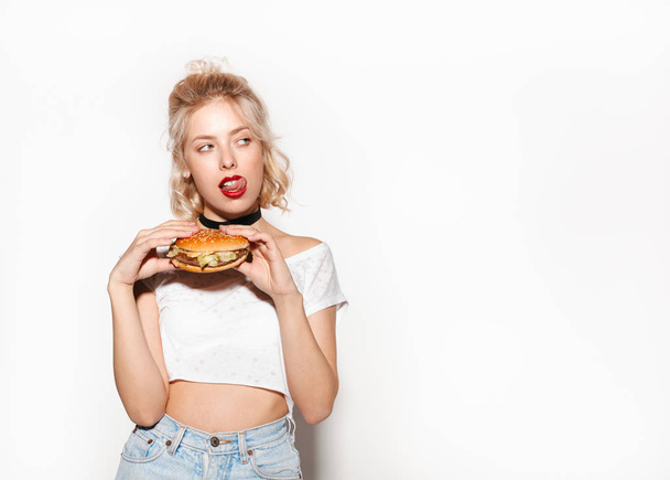 Woman holding burger and licking lips - Fotó, kép