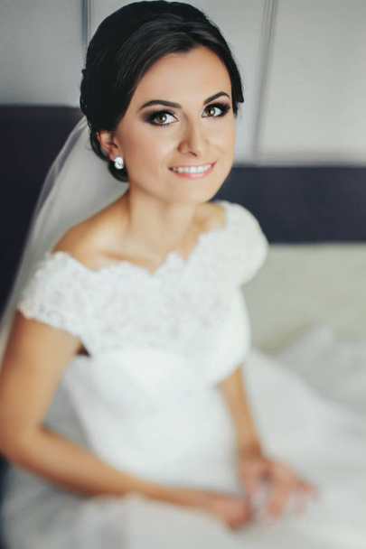 Brunette bride smiles sitting on the white bed  - Fotó, kép