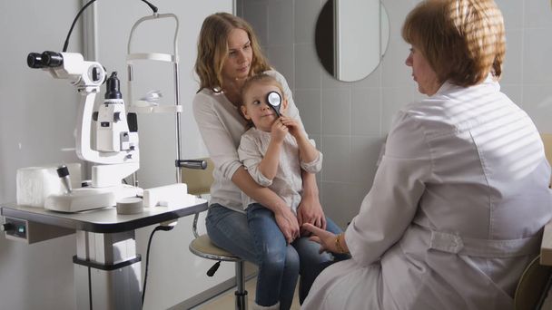 クリニックの眼科医は女の子視力について診断を説明 - 子供を果たしています。 - 写真・画像