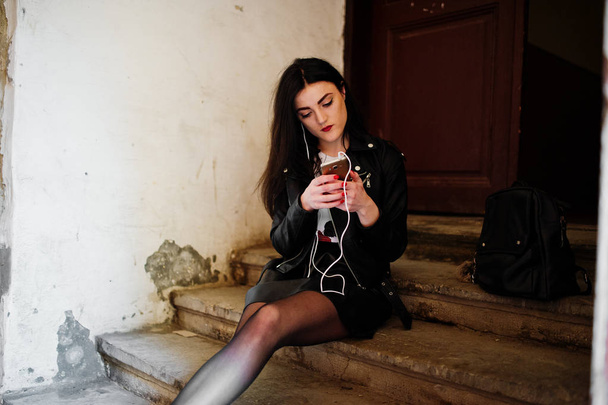 Young goth girl on black leather skirt and jacket sitting on sta - Foto, Imagen