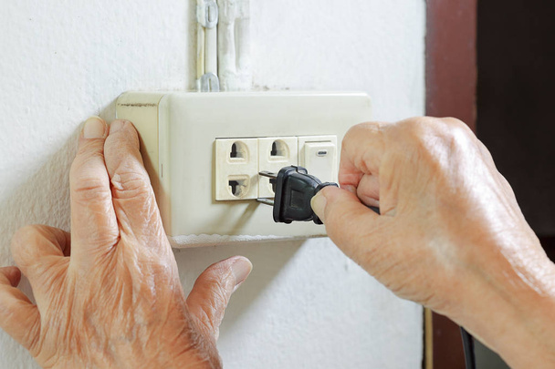 Elderly woman trying plug cable to the electric outlet - Photo, image