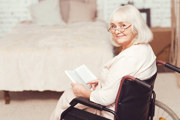 Charming retired lady reading book in wheelchair at home - Fotoğraf, Görsel