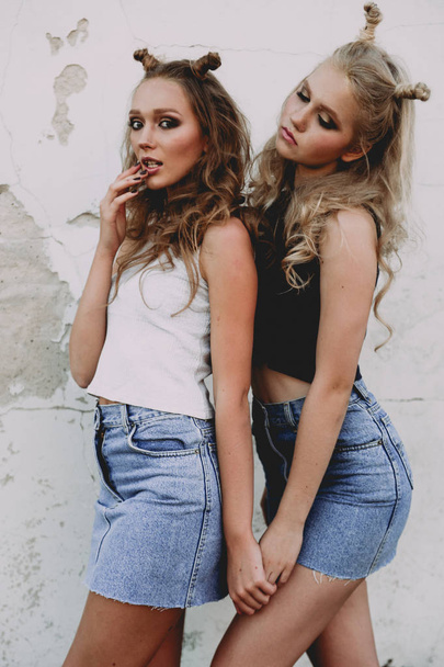 Lifestyle- und People-Konzept: Modeporträt zweier stilvoller Freundinnen in Jeansröcken, draußen auf dem Dach. fröhliche Sommerzeit zum Spaß. - Foto, Bild