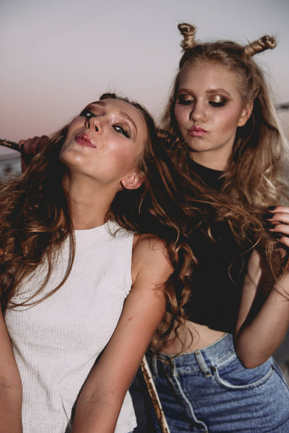 životní styl a lidé koncept: módní portrét dvou nejlepších přátel stylové dívky nosí džíny sukně, venku na střeše. Happy letní čas pro zábavu. - Fotografie, Obrázek