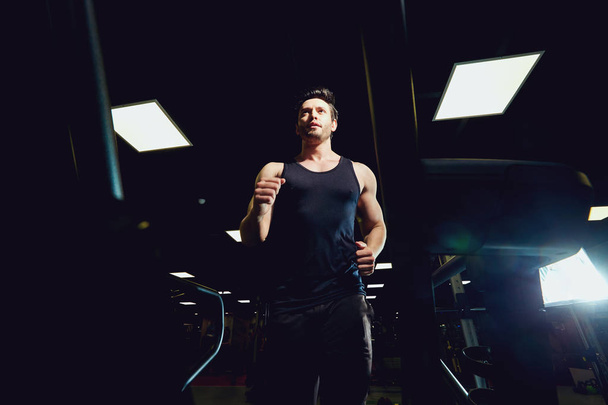 Man athlete runs jogging on a treadmill in dark gym - Foto, imagen