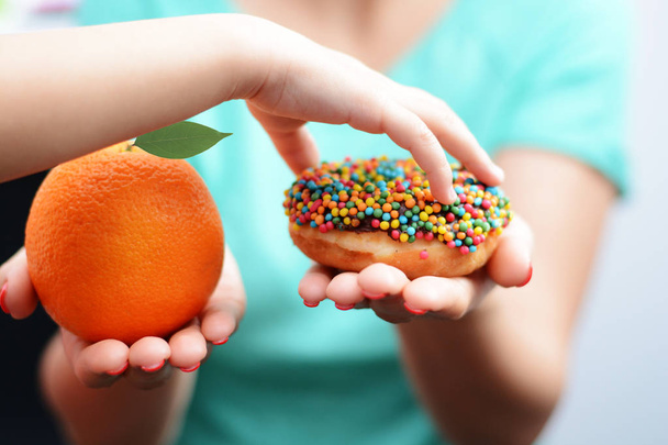 Koncepcja otyłość dziecka ręką dziewczynka wybór słodkich i niezdrowe pączka zamiast owoców - Zdjęcie, obraz