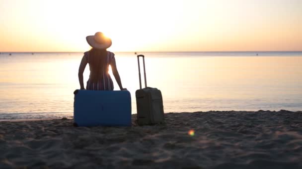 Een jonge vrouw zit op een koffer in de buurt van de zee - Video