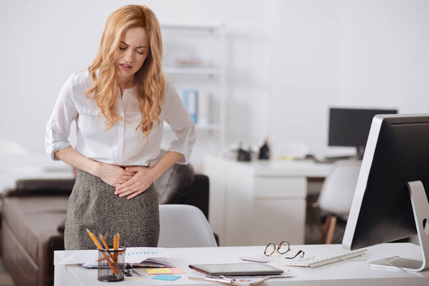 Miserly young businesswoman feeling stomachache in the office - Фото, изображение