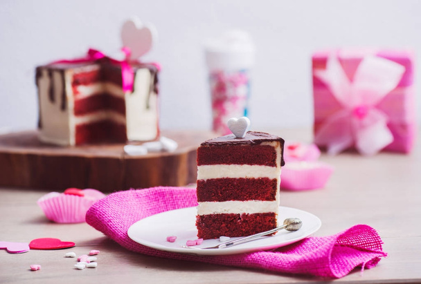 Slice of a red velvet cake and pink decoration around, present box in the background - Foto, Imagen
