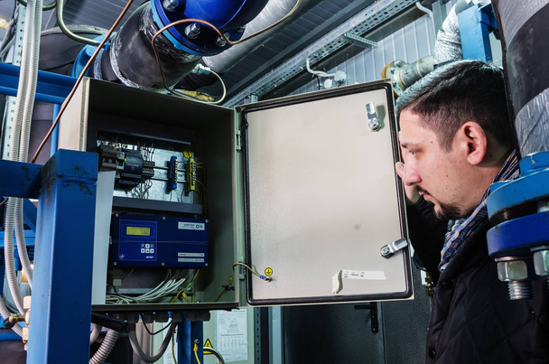Specialist examines the device for recording heat at a heat-regulating substation - Valokuva, kuva