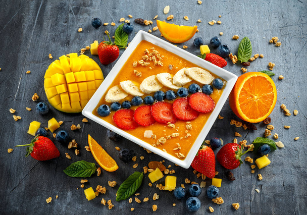 Свежий апельсиновый смузи на завтрак с черникой, мюсли, манго, клубникой и бананом
 - Фото, изображение