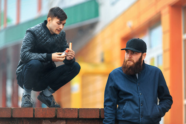 Vape. Two young people stand and smoke electronic cigarettes in the street on a cloudy day. - Valokuva, kuva