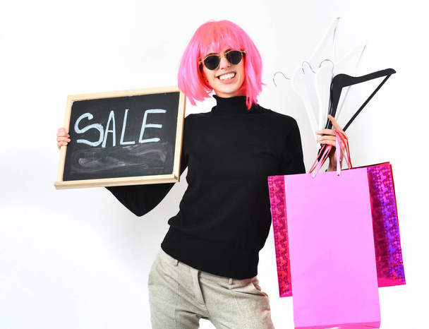 girl in wig holding package, hangers, board with sale inscription - Фото, изображение