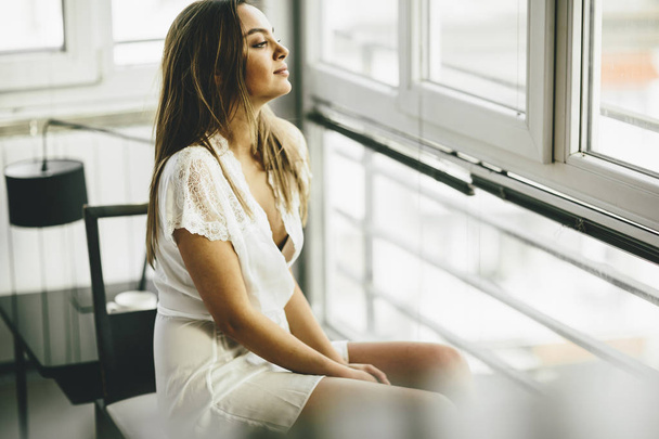 Молодая женщина сидит у окна
 - Фото, изображение