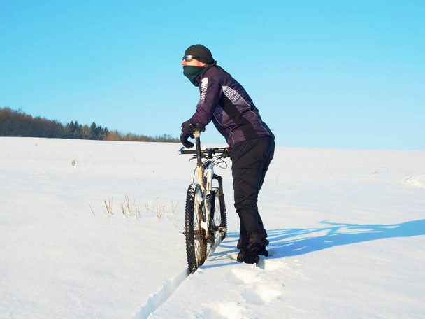 Motociclista empujando bicicleta de montaña en la nieve deriva. Clima frío y soleado de invierno. Motociclista está empujando bicicleta en nieve profunda
 - Foto, imagen