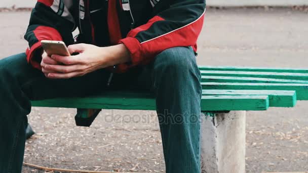 eenzaam in een rode jas is in het park zitten en iets te typen op een smartphone - Video