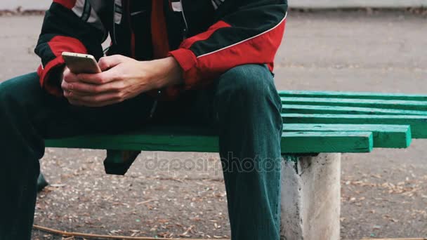 osamělý v červené sako je posezení v parku a cosi psal na smartphone - Záběry, video