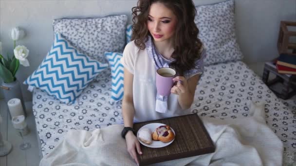 Mujer joven bebe café de la mañana y pasteles desayuno en el dormitorio
. - Imágenes, Vídeo