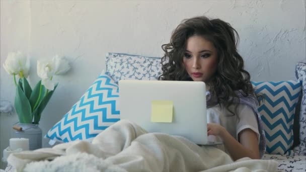 Een jonge vrouw onlangs wakker in bed en controleert de mail op de laptop. - Video